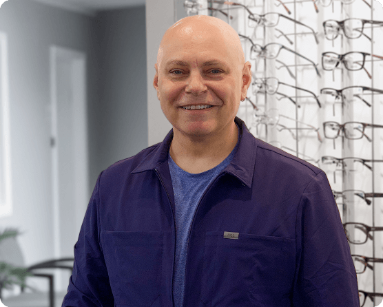 Dr. Brian Battaglia, Cheektowaga optometrist, smiling in front of a wall of eyeglasses at Value Vision.