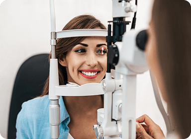 A smiling woman receiving an eye exam from an optometrist using a slit lamp microscope in a professional clinic.