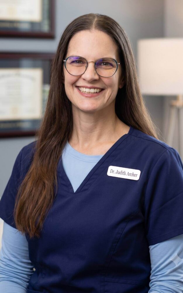Dr. Kalindi Desai, Williamsville optometrist, smiling in a white lab coat with eye exam equipment in the background.