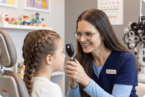 A smiling young girl wearing round glasses and a woman in an optical shop for a pediatric eye exam in Buffalo.